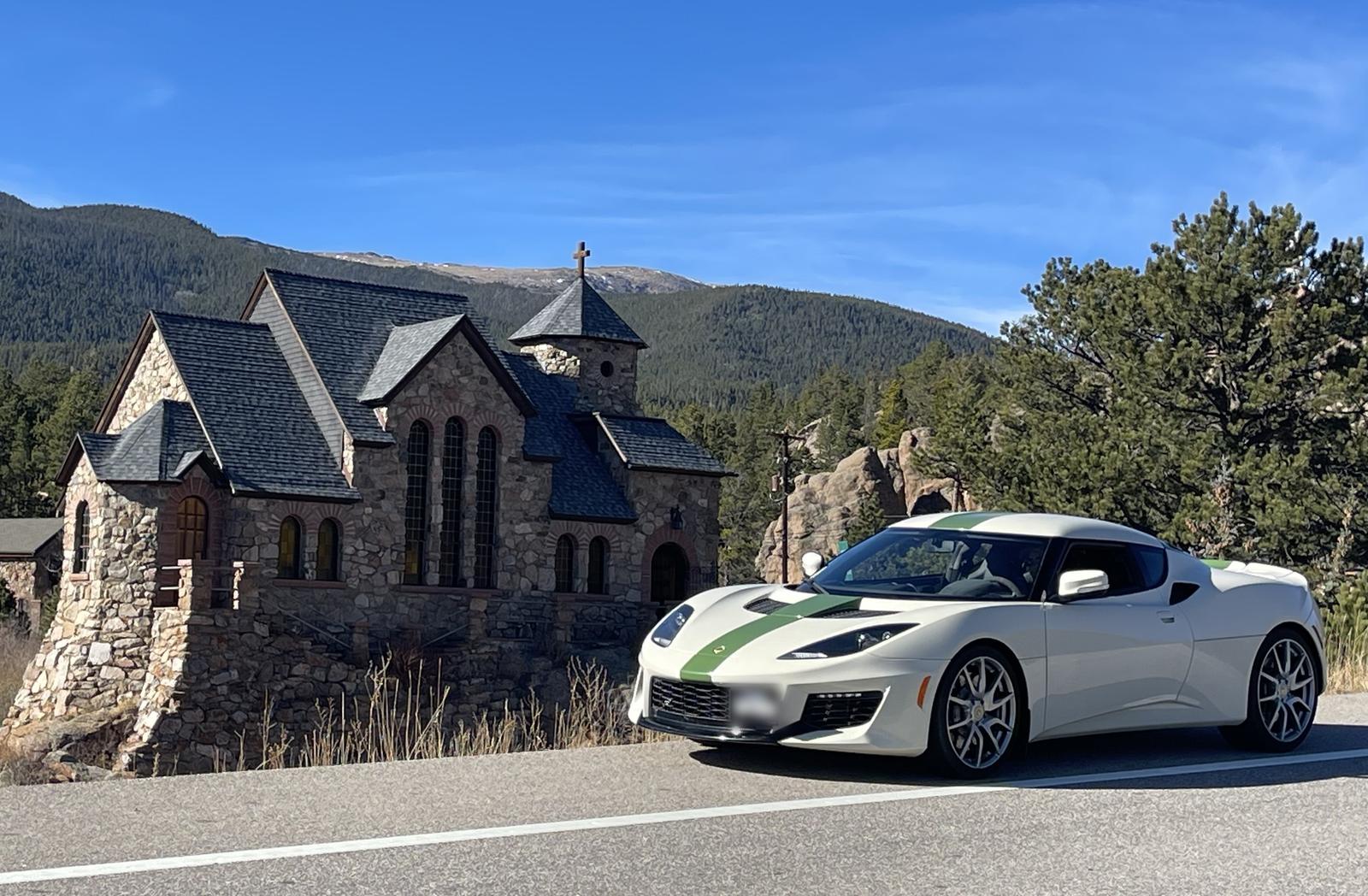 A white Lotus Evora with a green racing stripe on a Colorado mountain road